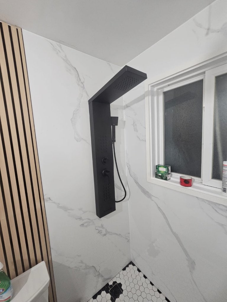 A finished shower with a matte black rain shower panel on marble-look walls, installed by Drain and Plumbing Solutions.